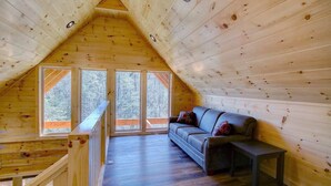 Una cabaña acogedora con habitación tipo buhardilla, piso de madera y sofá con cojines.