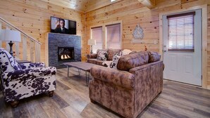 Un acogedor interior de cabaña con chimenea, paredes de madera, un televisor y un sofá.