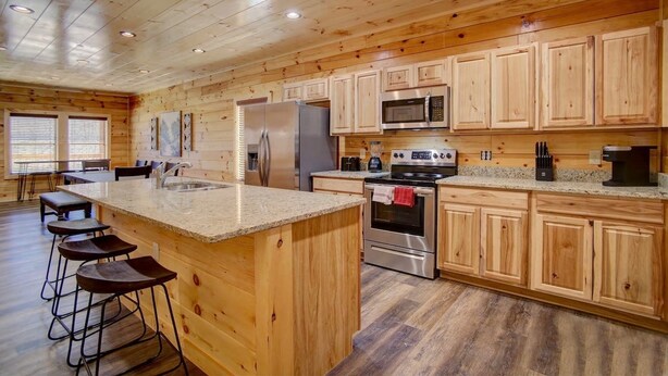 Una cocina amplia con armarios de madera, encimera de granito, electrodomésticos de acero inoxidable y una zona de bar con taburetes.
