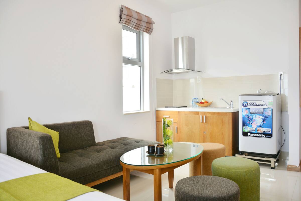 Une chambre d’hôtel moderne équipée d’un canapé, d’une table en verre, d’une kitchenette et d’un réfrigérateur Panasonic.
