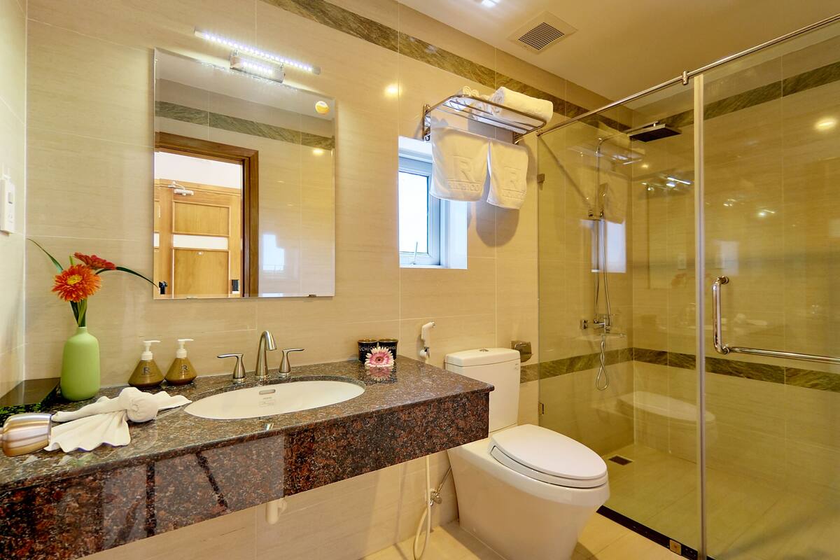 Une salle de bain moderne avec un comptoir en granit, un lavabo, des toilettes et une douche à parois de verre.