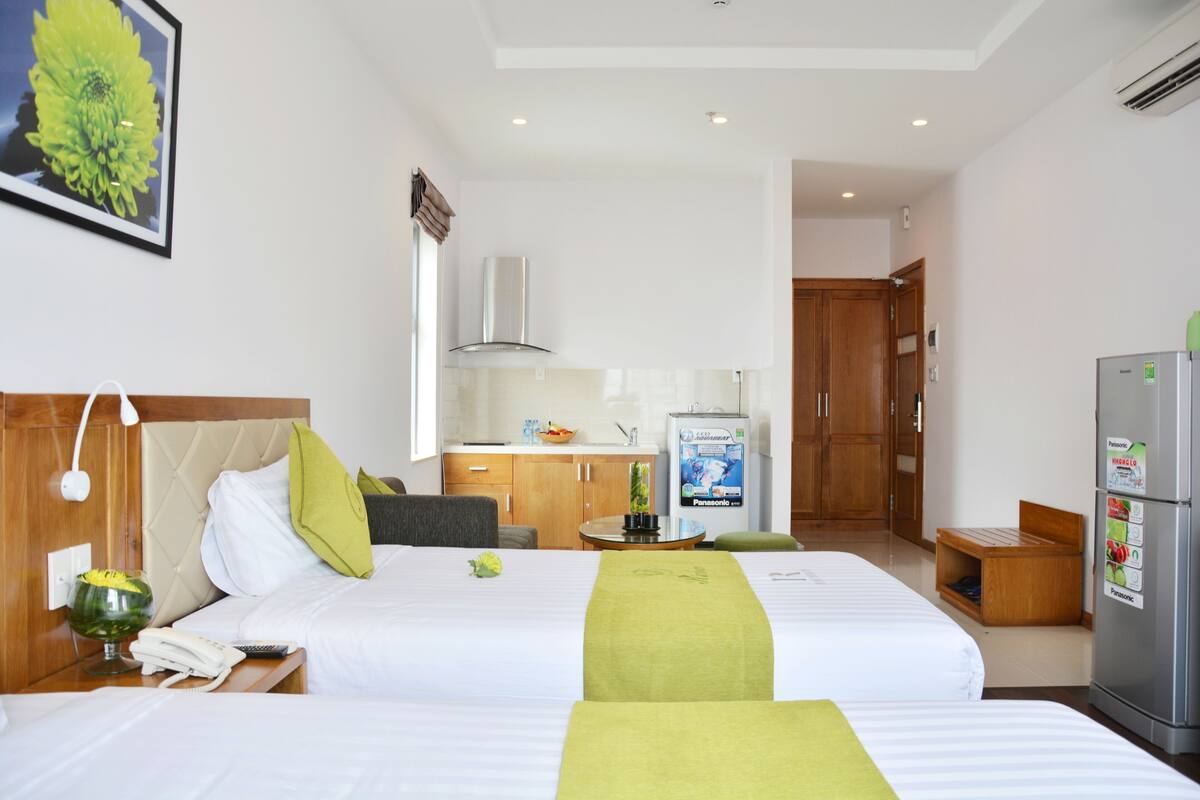 Une chambre d’hôtel avec deux lits, une kitchenette, un réfrigérateur et une salle de bain visible à travers une porte ouverte.