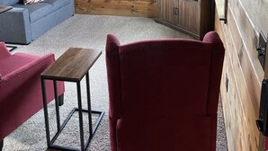 A cozy cabin interior with a wooden ceiling, a blue sofa, a red armchair, a small table, and a television on a wooden cabinet. - Camas Creek Cottage (Hamilton)