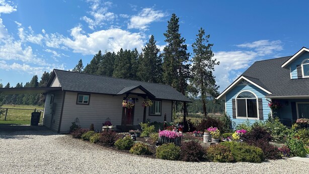 A two-story house with a gravel driveway, surrounded by a variety of potted plants and flowers. - Camas Creek Cottage (Hamilton)