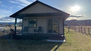 A small, single-story house with a porch, a sliding glass door, and a fenced yard. - Camas Creek Cottage (Hamilton)