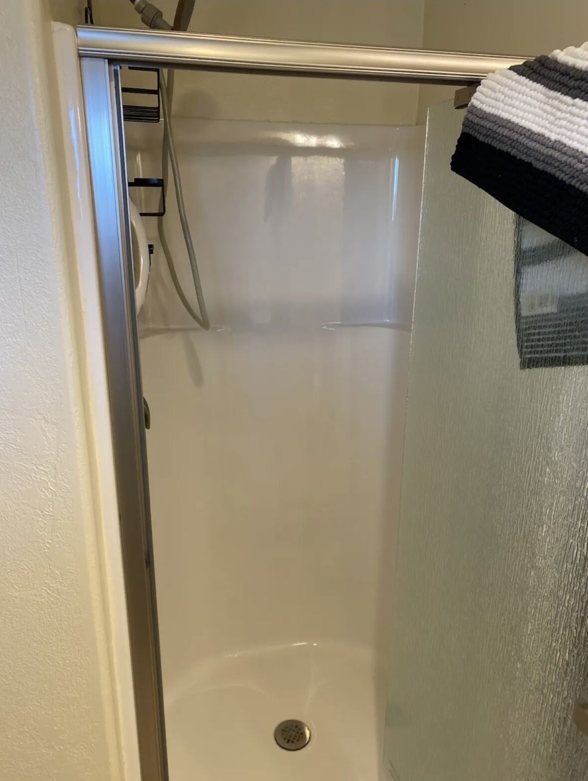 Un baño con cabina de ducha de vidrio, pared blanca y una toalla colgada a la derecha.