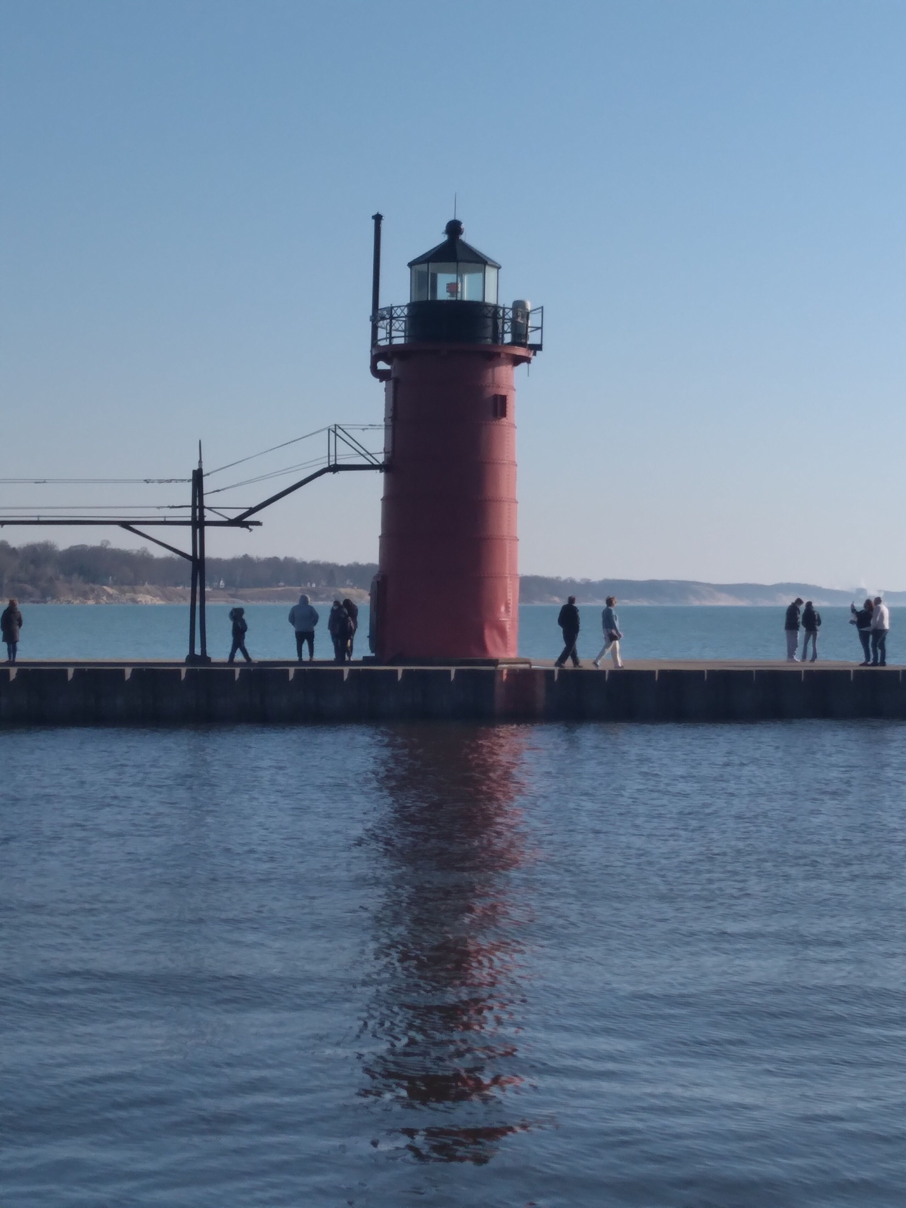 Un faro rojo con un camino que lleva a él, con vista a aguas tranquilas.