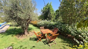 Un giardino con tavolo e sedie in legno, circondato da piante e fiori.