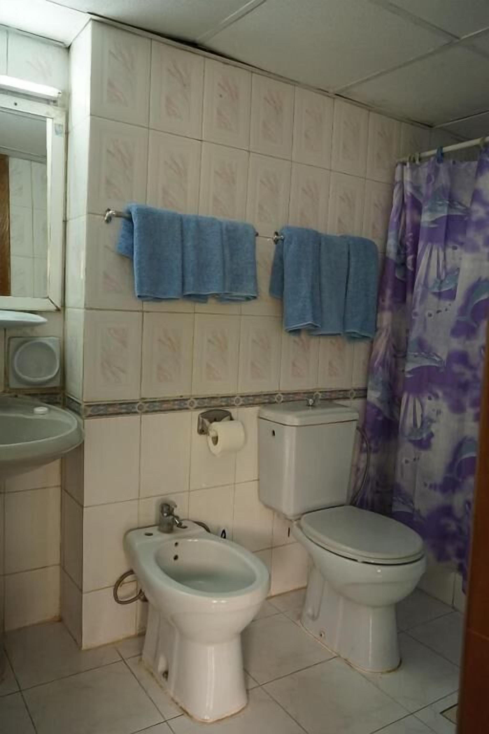 A bathroom with a toilet, bidet, and sink. There are blue towels hanging on the wall.