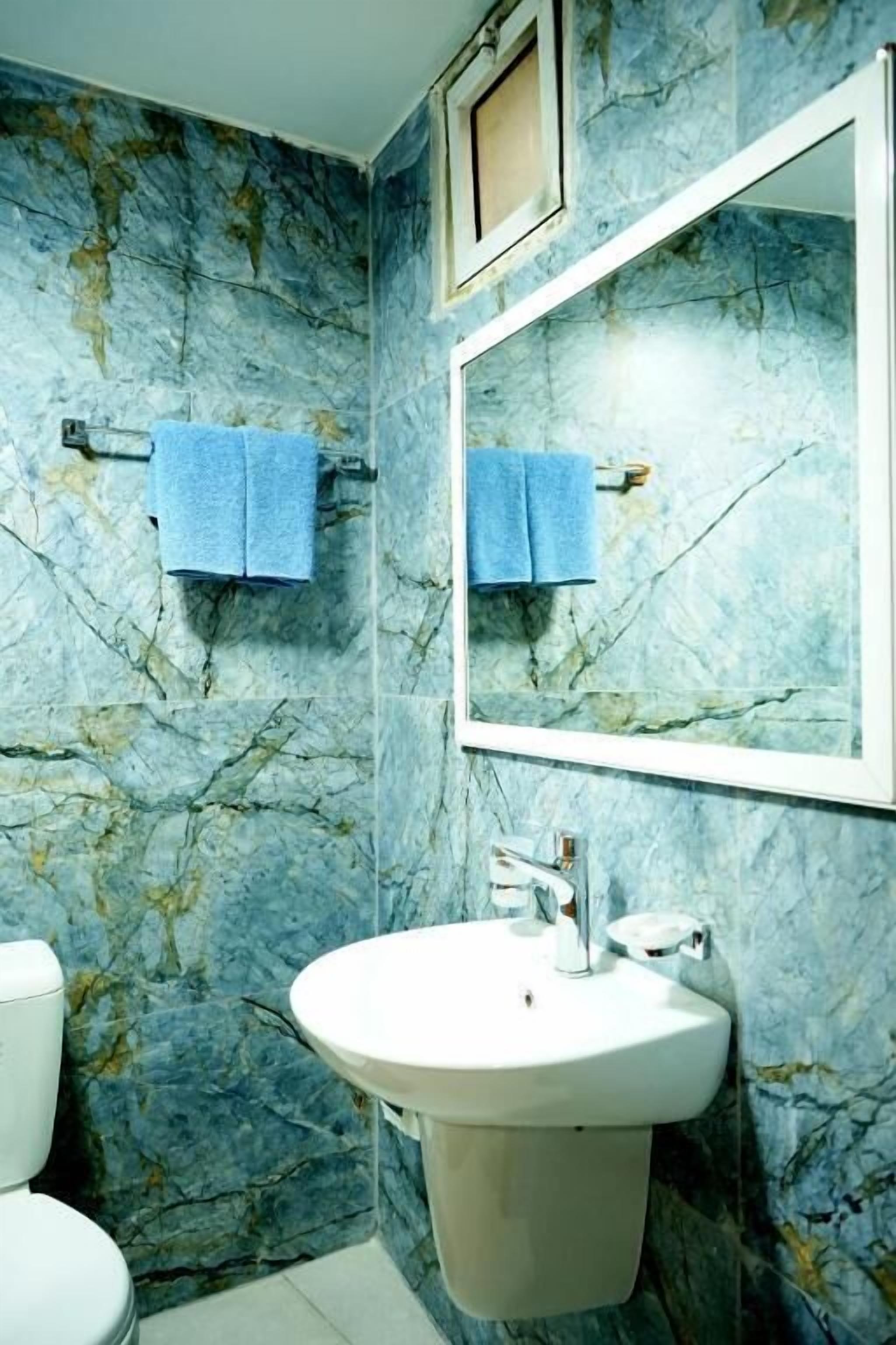 A bathroom with a marble wall, a sink, a mirror, and two towels hanging on hooks.