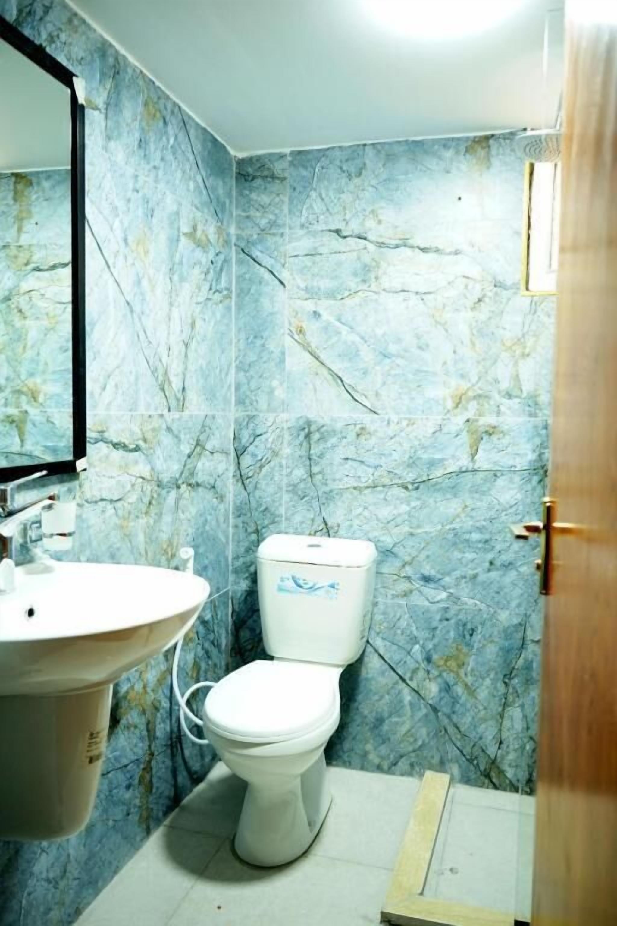 Un baño con pared de mármol, lavamanos e inodoro.