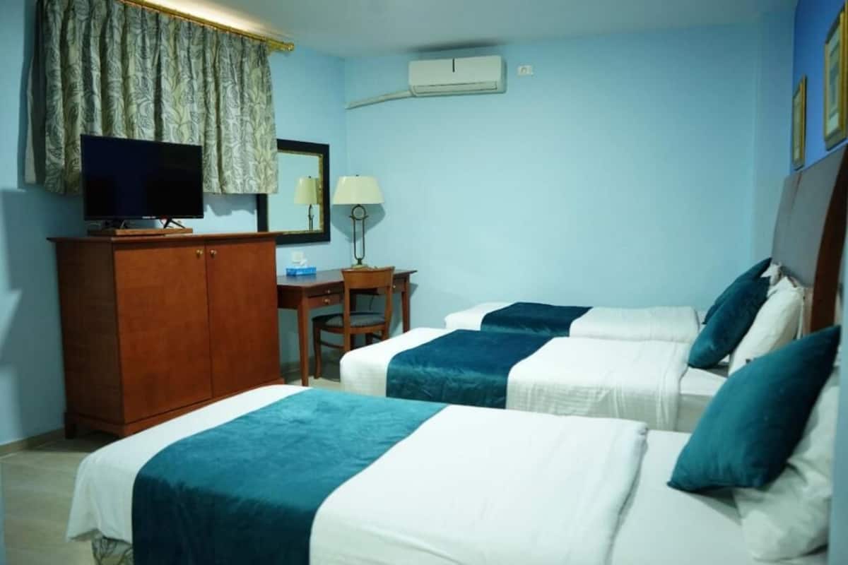 A hotel room with two beds, a television, a desk with a lamp, and an air conditioning unit.
