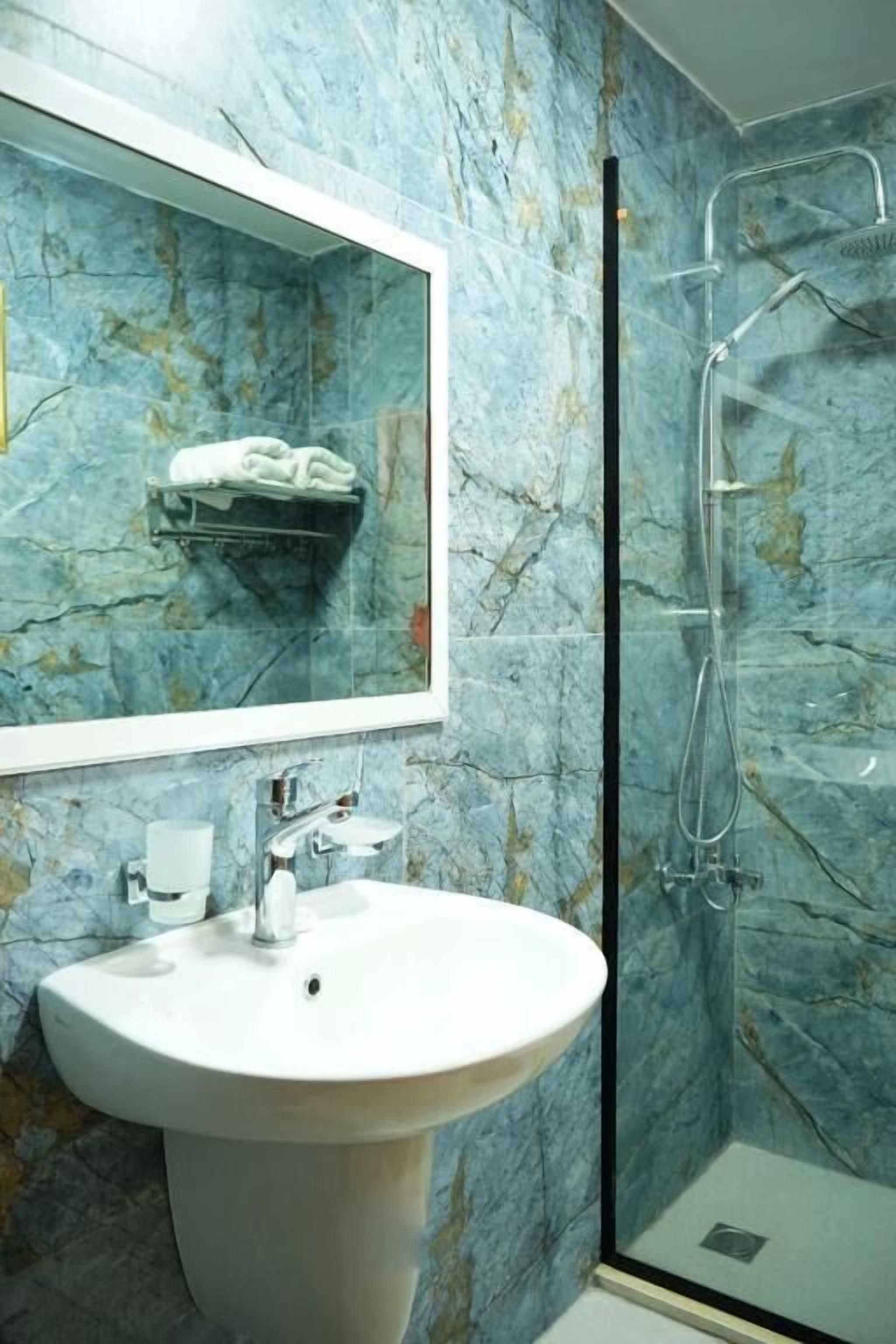 A bathroom with a marble wall, a sink, a mirror, and a shower enclosure.