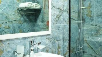 A bathroom with a marble wall, a sink, a mirror, and a shower enclosure.