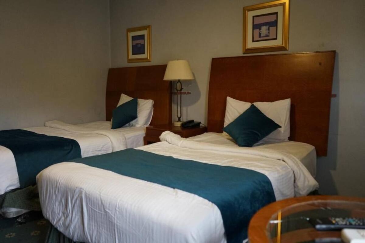 A hotel room with two single beds, each with a headboard, a bedside table, and a lamp.
