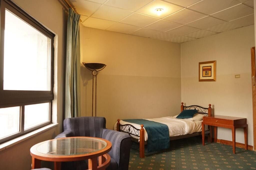 Een compacte, verzorgde slaapkamer met een enkel bed, een stoel, een klein tafeltje en een vloerlamp.