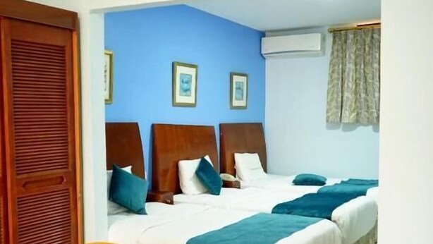 A hotel room with two beds, a wooden chair, and a blue wall. - Concord hotel  (Amman)