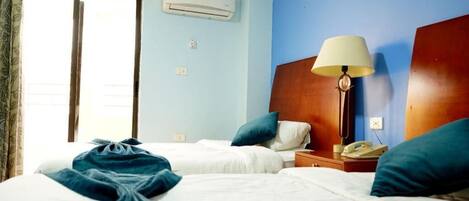 Habitación de hotel con dos camas, una mesita de noche con lámpara, aire acondicionado y una ventana con cortinas.