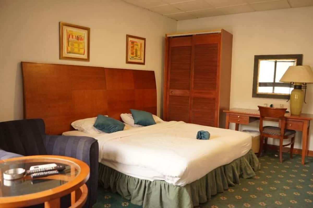 A hotel room with a bed, a desk, a chair, a lamp, and two framed pictures on the wall.