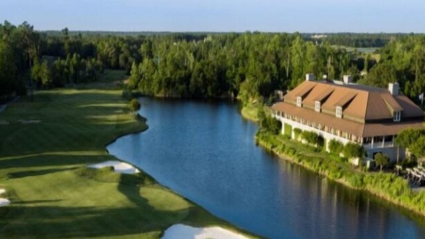 A golf course with a clubhouse and a body of water.