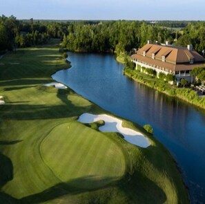 A golf course with a clubhouse and a body of water.