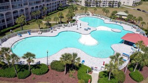 A large, irregularly shaped pool with multiple sections, surrounded by a white fence and palm trees.