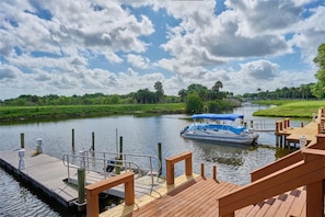 A wooden dock with a boat, a calm river, and a grassy bank with trees.