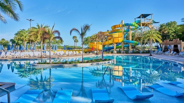 A swimming pool with water slides, lounge chairs, and palm trees.