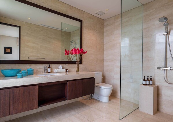 Une salle de bain moderne dotée d’une douche à parois de verre, d’un grand miroir et d’un meuble-lavabo avec un plan de travail de couleur beige.
