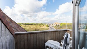 A balcony with a view of a road and greenery, a wooden wall, and two white chairs.