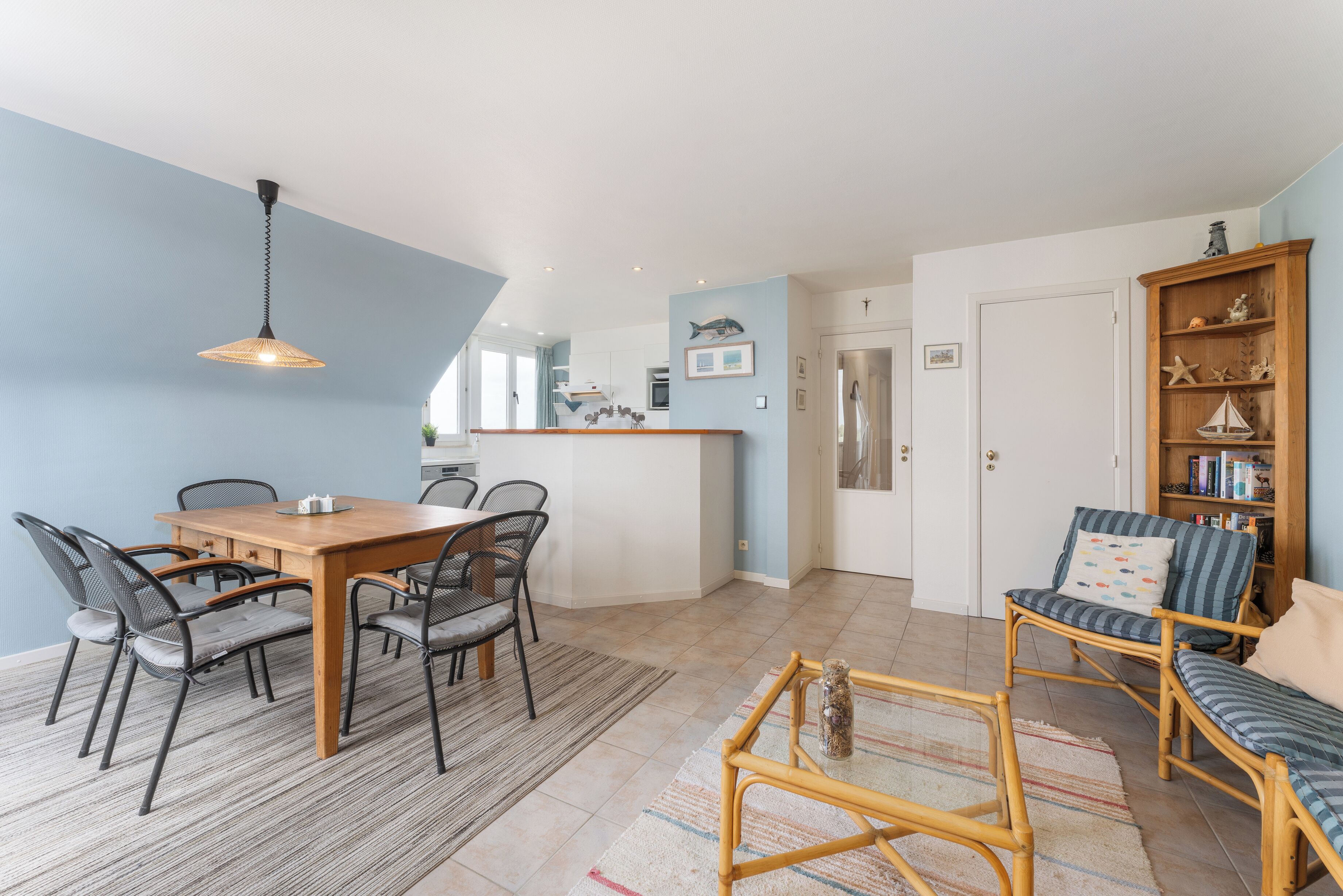 Eine moderne Küche mit einer zentralen Kochinsel, Essbereich mit Holztisch und Stühlen sowie eine Sitzecke mit Sofa und Sesseln.