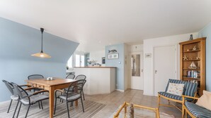 A modern kitchen with a central island, dining area with a wooden table and chairs, and a seating area with a sofa and armchairs.