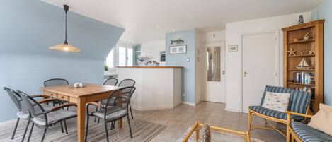 Eine moderne Küche mit einer zentralen Kochinsel, Essbereich mit Holztisch und Stühlen sowie eine Sitzecke mit Sofa und Sesseln.