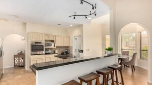 A modern kitchen with a central island, bar stools, and a dining area with a table and chairs.