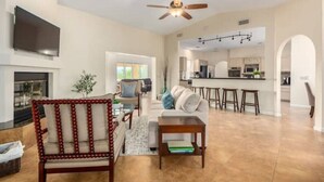 A spacious living room with a fireplace, a dining area, and a kitchen in the background.