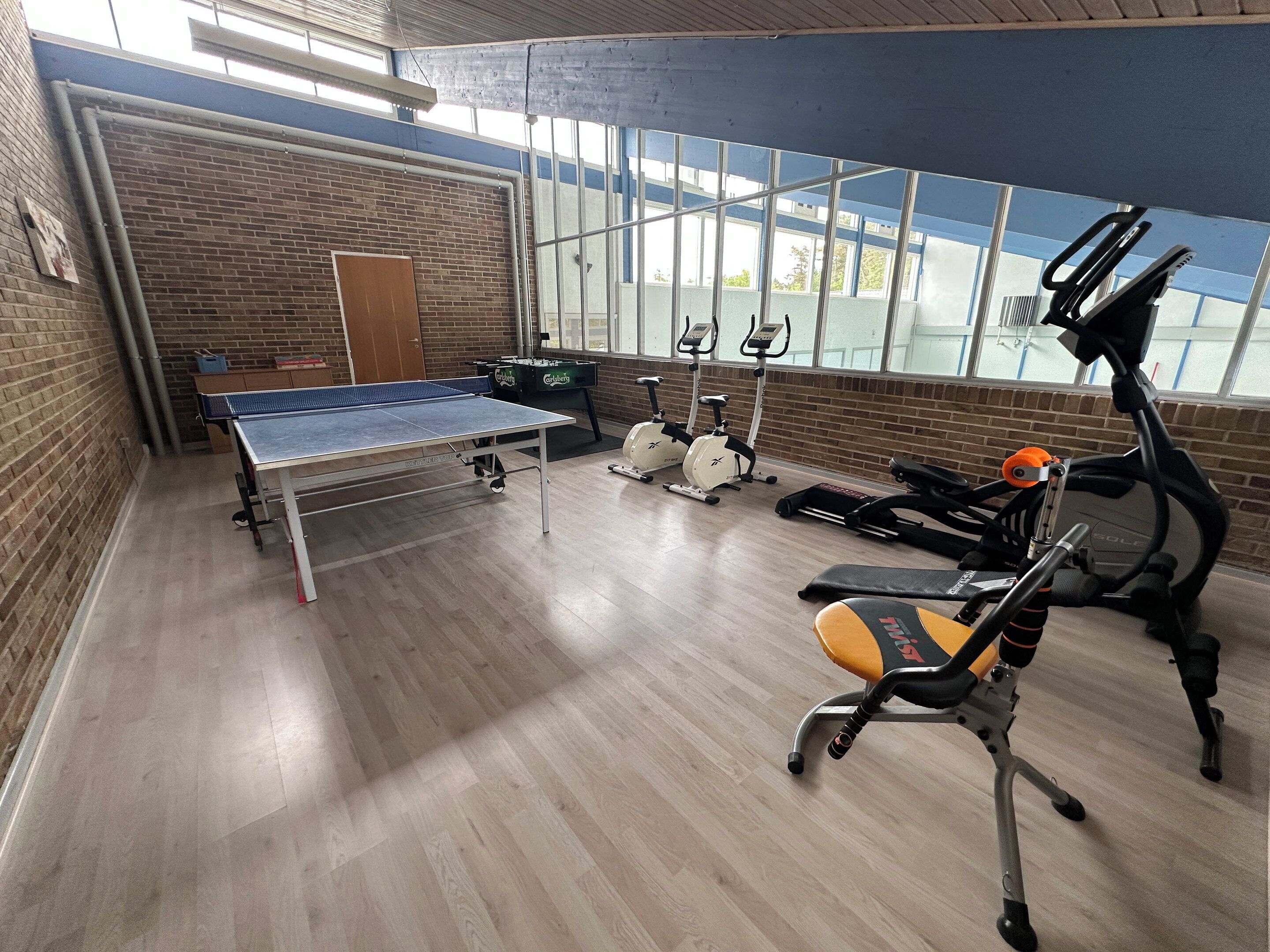 A gym with a ping pong table, stationary bikes, and a treadmill.