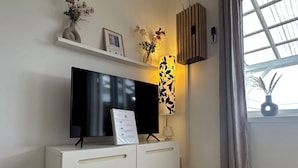Una sala moderna con una televisión de pantalla plana sobre un mueble blanco, un adorno de pared y un ventanal con cortinas.