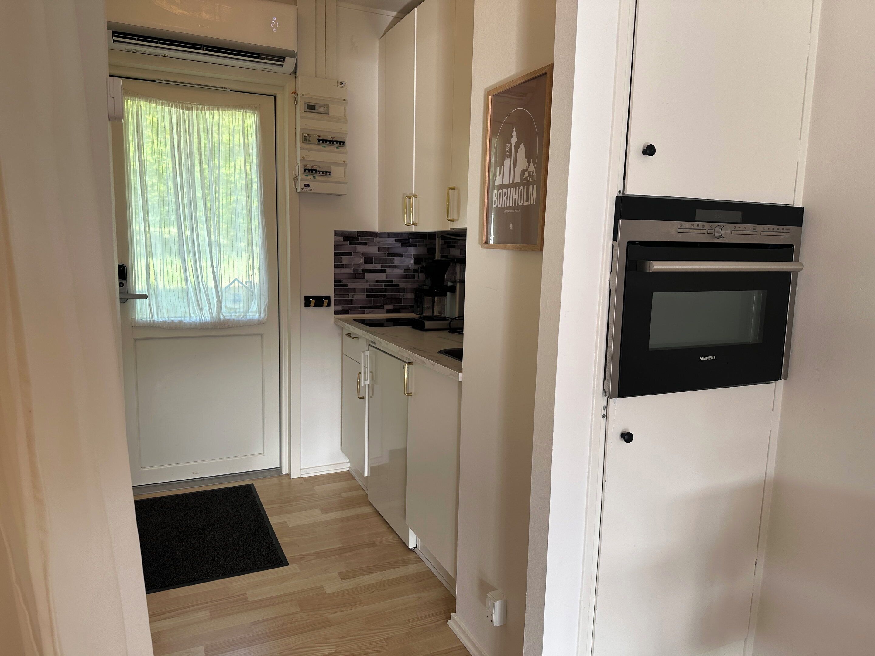 A compact kitchen with a built-in oven, a window with curtains, and a tiled backsplash.