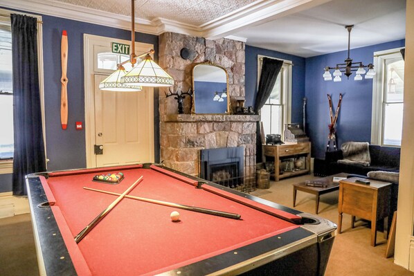 A pool table with cues, a fireplace, a sofa, and a door marked "EXIT". - The Saucy Willow Inn and Cottages (Kawartha Lakes)