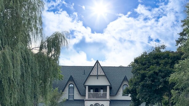A large, two-story house with a balcony, surrounded by a well-maintained lawn and dock with chairs.