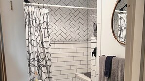 A bathroom with a white toilet, a shower with a black and white patterned shower curtain, and a tiled floor with a hexagonal pattern.