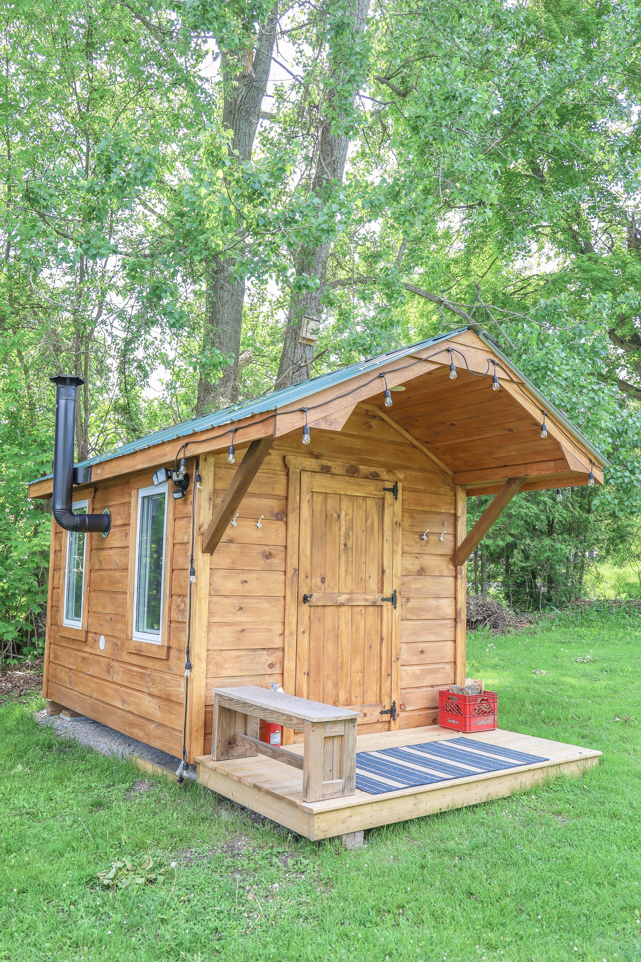 A wooden cabin with a sloped roof, a chimney, a small porch, and a window.