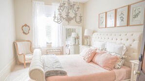 A bedroom with a large bed, a chair, a dresser, and a chandelier.