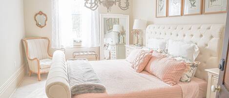 A bedroom with a large bed, a chair, a dresser, and a chandelier.