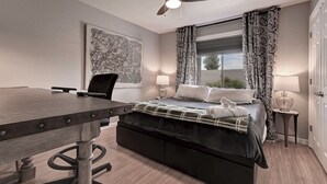 A modern bedroom with a bed, a desk, a chair, a ceiling fan, and a window with curtains. - Charming & Comfy Condo in the Heart of Old Town! (Scottsdale)
