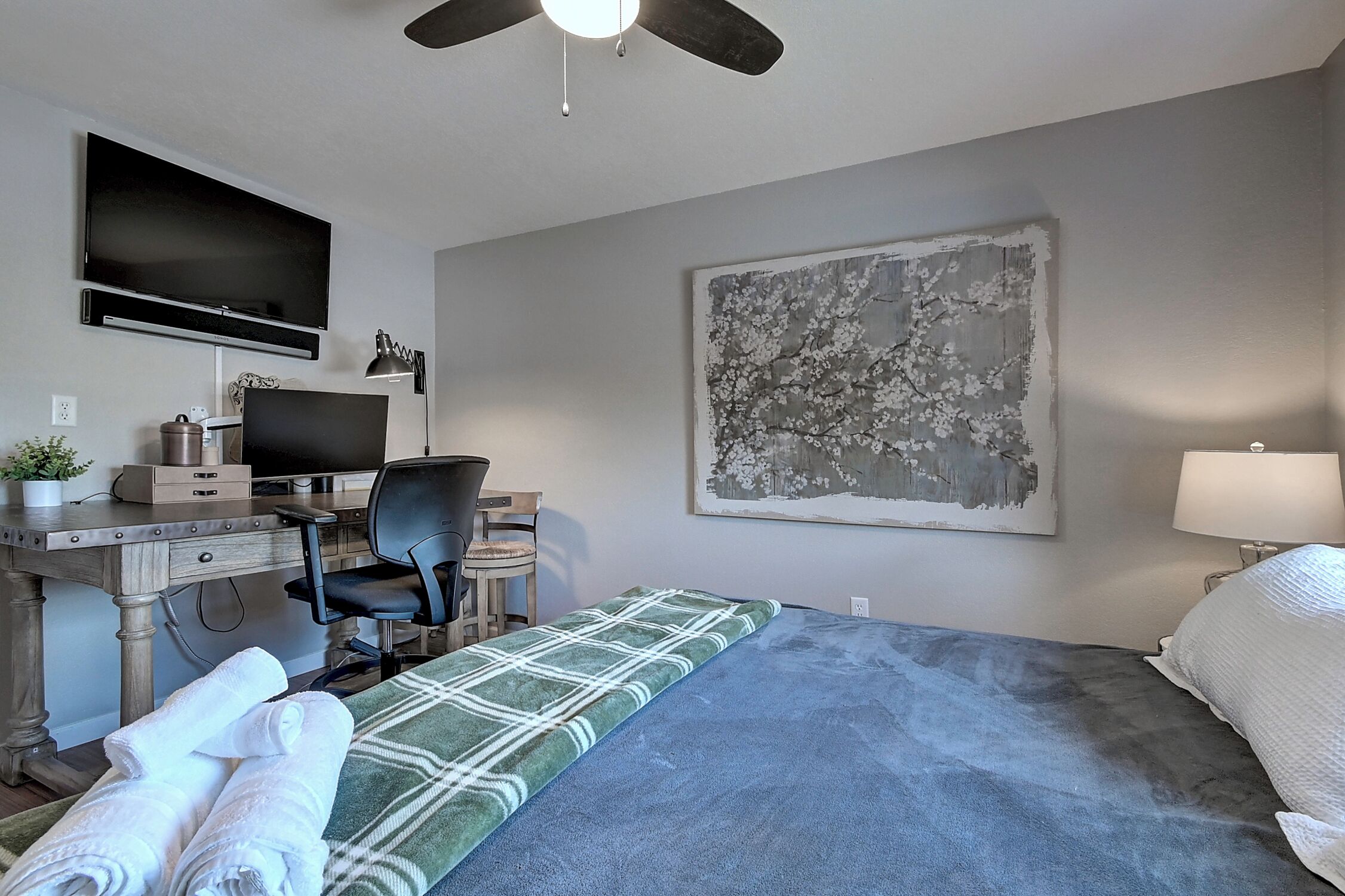 Une chambre d’hôtel avec un lit, un bureau équipé d’un ordinateur, une chaise, une télévision et un grand tableau accroché au mur.