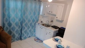 Een kleine keuken met witte kastjes, een spoelbak en een aanrecht met blauwe borden.