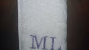 Een witte handdoek met de letters “ML” geborduurd.