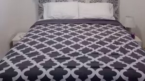 Een slaapkamer met een bedovertrek met patroon, een wit hoofdeinde en een plafondlamp.