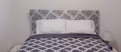 Une chambre à coucher avec une couvre-lit à motifs, une tête de lit blanche et un luminaire au plafond.